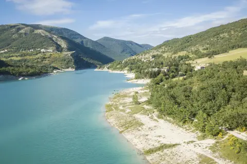 Spiaggia libera sul lago di Fiastra, con acque turchesi e montagne verdi sullo sfondo. Un luogo ideale per rilassarsi e godersi la natura.