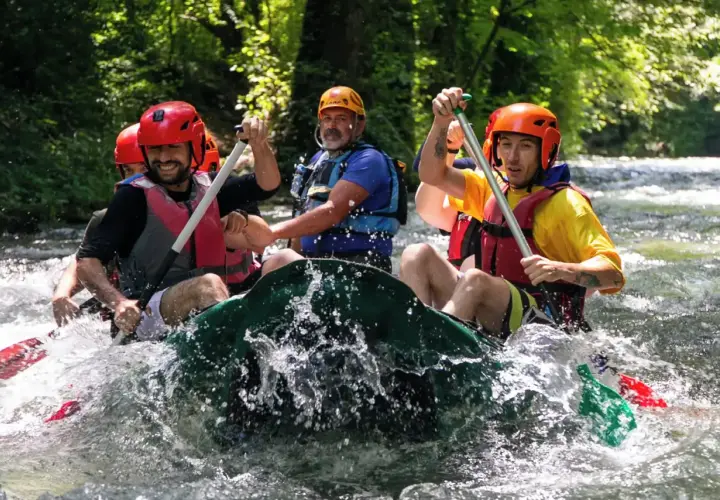 Un gruppo di amici si diverte in un'avventura di rafting nelle Marche, pagaiando con entusiasmo tra le rapide.