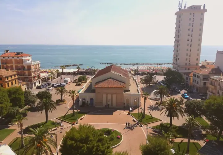 Piazza centrale con teatro, palazzi, palme e mare sullo sfondo. Ecco cosa vedere a Porto Recanati.