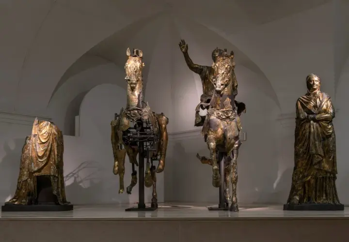 Statue equestri e figure umane in bronzo dorato, un'antica **pergola** che evoca le Marche.