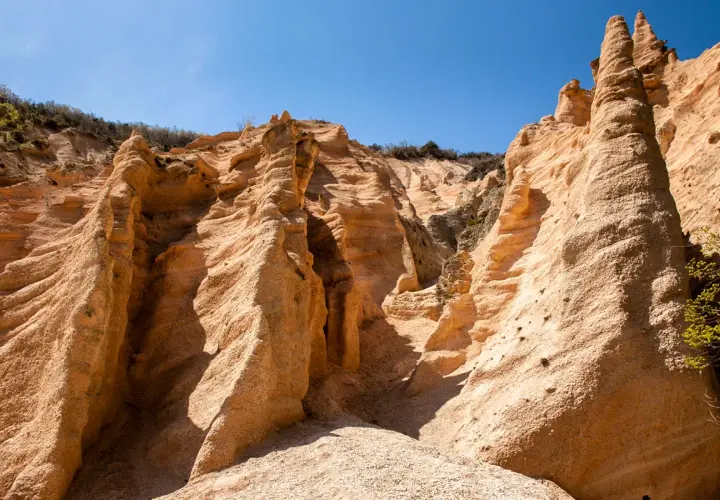 Formazioni rocciose color ocra, scolpite dal vento, sembrano **le lame rosse** di un canyon desertico sotto un cielo azzurro intenso.