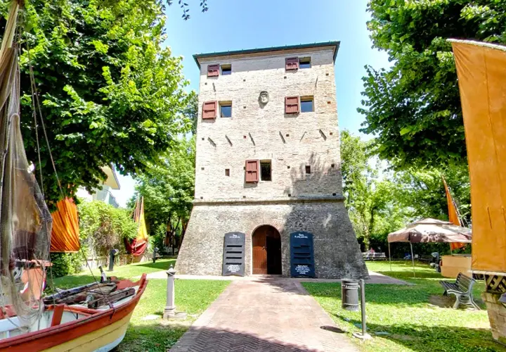 Torre dell'orologio nel centro storico di Igea Marina, con barche e bandiere colorate.