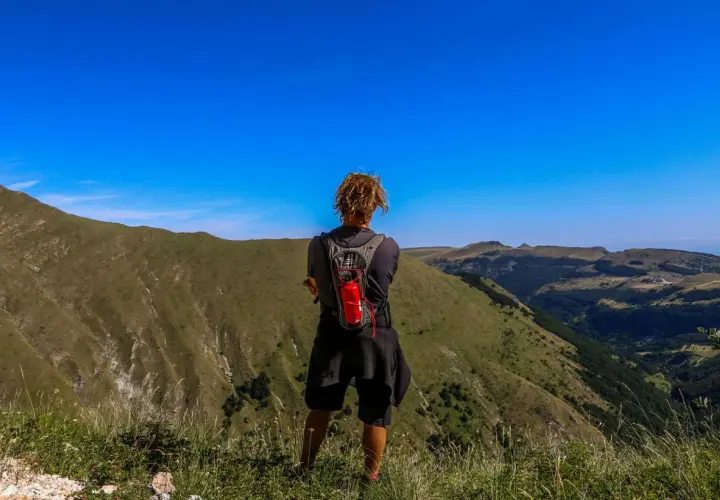 Persona con zaino ammira il panorama durante un trekking di 3 giorni nei Monti Sibillini.