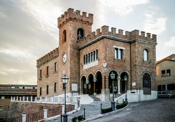 Edificio storico in mattoni a Mondolfo, cosa vedere: torre con orologio, archi e scalinata.