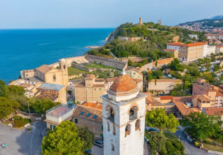 Vista aerea del **centro storico** di Ancona, con il mare blu, chiese, torri e case con tetti rossi.