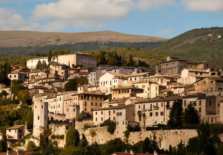 Spello, un borgo umbro incastonato tra colline verdi, con case in pietra e torri antiche che si stagliano contro il cielo azzurro.