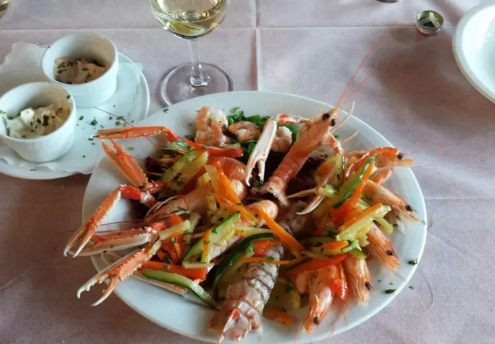Un piatto di scampi e gamberi con verdure miste, un bicchiere di vino bianco e salse, un'ottima cena al conte Max Monte Roberto.