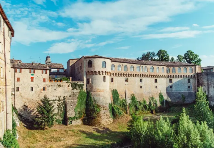 Un imponente palazzo storico con torri e mura di mattoni, circondato da vegetazione. Un luogo da scoprire: Urbania cosa vedere.