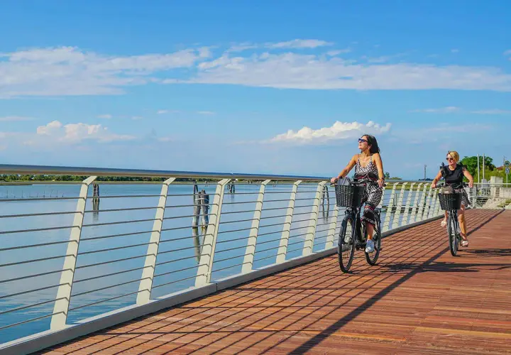 Due donne in bicicletta su una moderna pista ciclabile jesi, con il mare e il cielo azzurro sullo sfondo.
