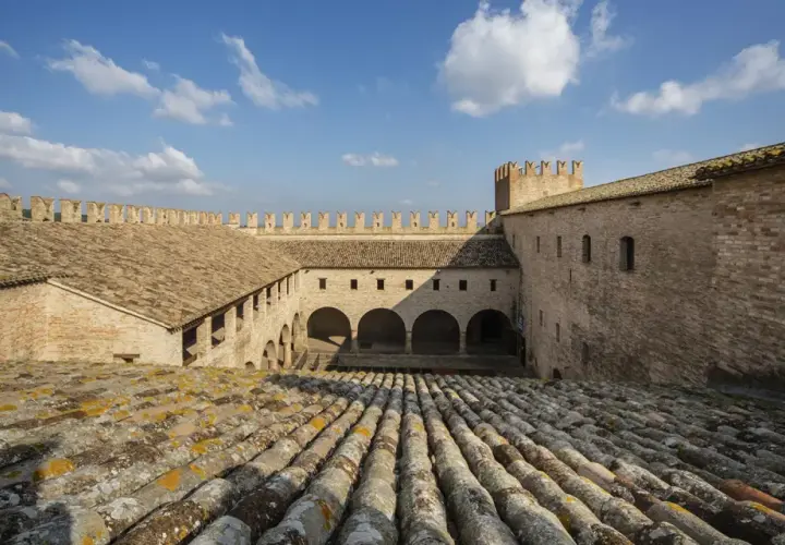 Cortile interno di un castello a Tolentino, Marche, con tetti in cotto e cielo azzurro.