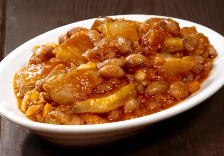 Piatto fumante di fagioli con le cotiche, un classico della ricetta marchigiana, servito in una ciotola bianca su un tavolo di legno scuro.