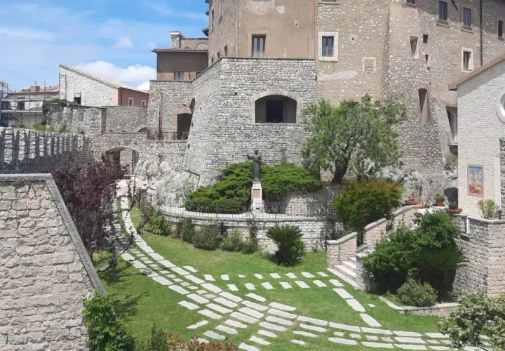 Un angolo suggestivo del centro storico di Rieti, con antiche mura in pietra, un giardino curato e una statua.