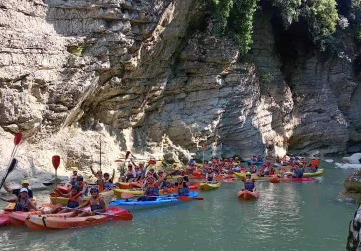 Gente in kayak esplora un canyon con pareti rocciose imponenti, simili a marmitte dei giganti nelle Marche.