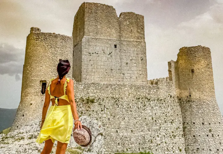 Donna in abito giallo ammira la Rocca Calascio, un luogo da non perdere per la sua storia e panorami mozzafiato.