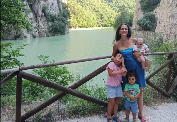 Famiglia felice nella golena del Furlo, con un lago turchese e montagne verdi sullo sfondo.