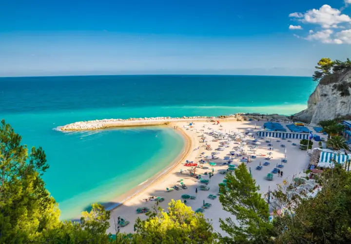 Spiagge Sirolo con acque turchesi, sabbia dorata, ombrelloni e gente che si gode il sole.