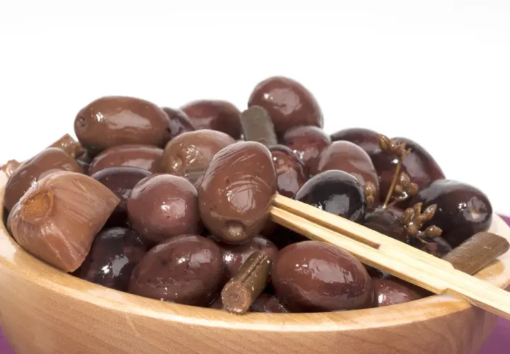 Olive nere sotto sale, un assaggio della ricetta marchigiana. Un piatto di olive scure e lucide in una ciotola di legno.