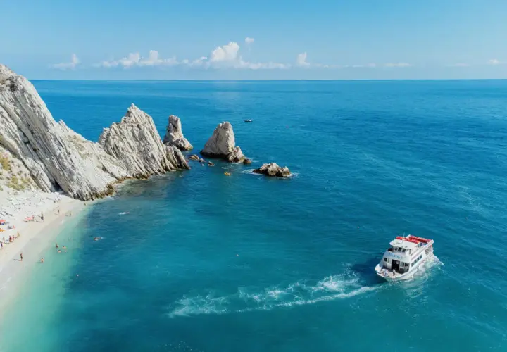 La spiaggia delle Due Sorelle, con le sue iconiche rocce, accoglie bagnanti e kayak. Una barca solca il mare azzurro.