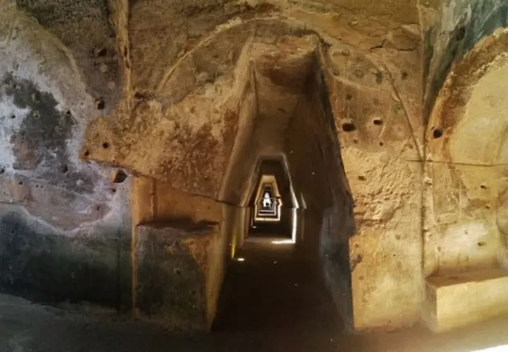 Interno della grotta della Sibilla: un corridoio stretto e trapezoidale scavato nella roccia, con nicchie e aperture.