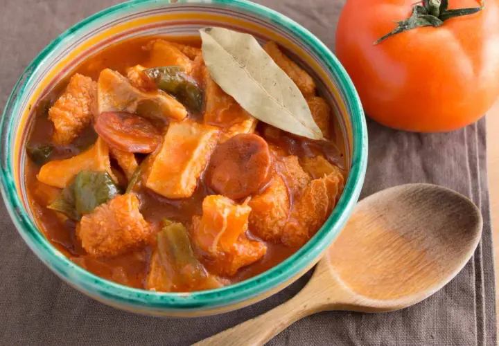 Un invitante piatto di trippa alla marchigiana, con peperoni e pomodoro, pronto per essere gustato con un cucchiaio di legno.