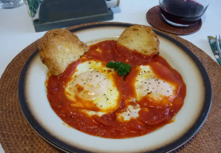 Uova in trippa marchigiana, un piatto saporito con uova in camicia su un letto di sugo rosso, guarnito con pane tostato e prezzemolo.