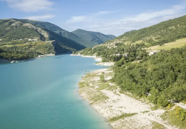 Spiaggia libera sul lago di Fiastra, con acque turchesi e montagne verdi sullo sfondo. Un luogo ideale per rilassarsi e godersi la natura.