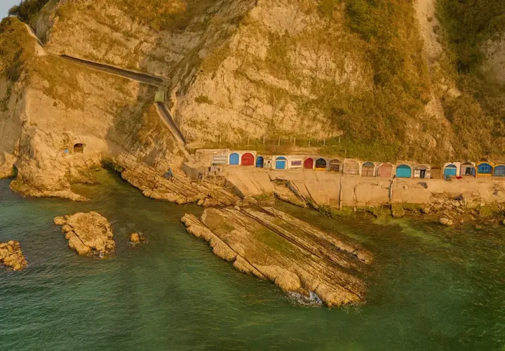 Piccole casette colorate a ridosso della scogliera, con il mare verde smeraldo che lambisce le rocce. Un angolo di paradiso vicino alla grotta azzurra di Ancona.