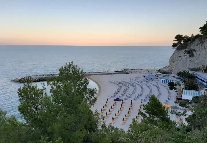 Spiaggia ordinata con lettini e ombrelloni, ideale per scoprire cosa vedere a Numana e Sirolo. Mare calmo al tramonto.