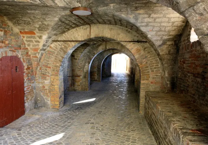 Arco in mattoni a Corinaldo, cosa vedere: un suggestivo passaggio coperto con pavimentazione in pietra e una porta rossa.