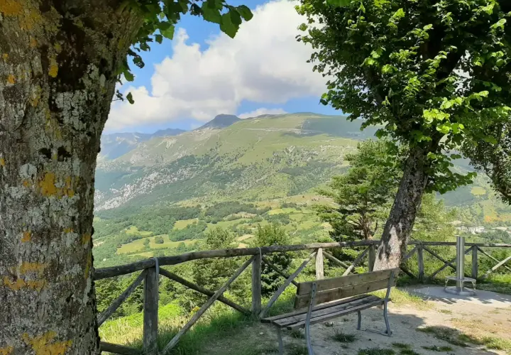 Panoramica mozzafiato del monte Monaco nelle Marche, con un sentiero serpeggiante e un cielo azzurro con nuvole bianche.