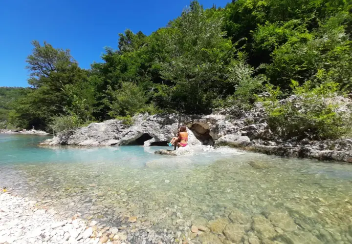 Bambini giocano nel **genga fiume** dalle acque cristalline, circondato da rocce e vegetazione lussureggiante.