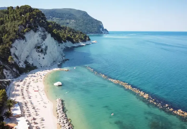 Spiaggia affollata con ombrelloni e lettini, scogliere bianche e mare azzurro a Porto Sant'Elpidio Mare.