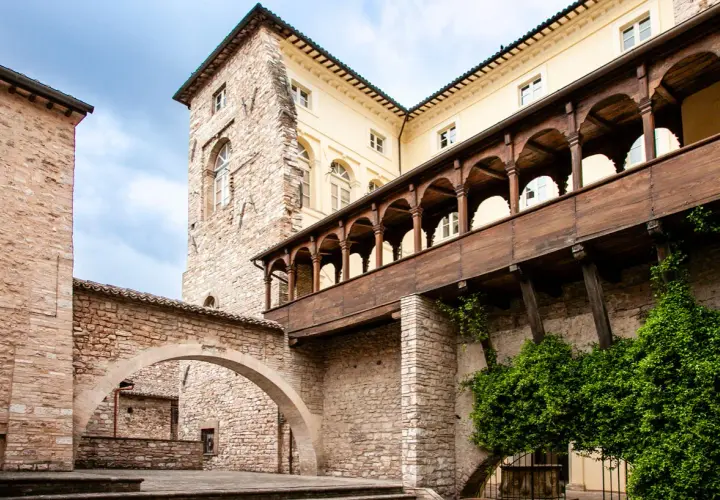 Cortile storico con archi in pietra e un loggiato in legno. Un assaggio di cosa vedere a Spello in un giorno, tra storia e natura.