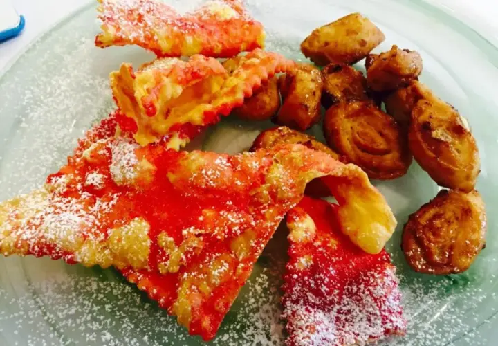 Cresciole marchigiane di Benedetta, dolci fritti cosparsi di zucchero a velo, con un tocco di rosso vivace.