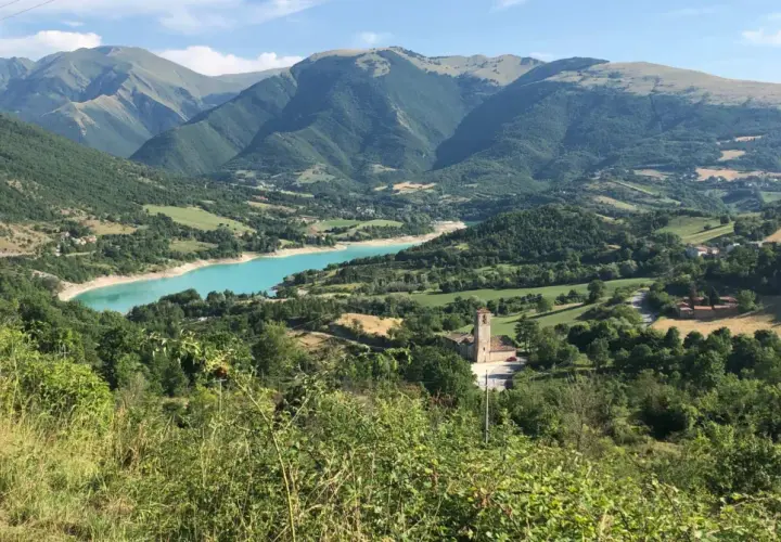 Panoramica del lago di Fiastra, con montagne verdi, un borgo e una chiesa. Cosa vedere in questo paesaggio mozzafiato.