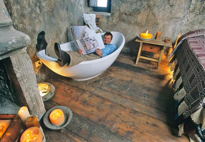 Uomo rilassato in vasca da bagno, legge un libro in un ambiente rustico, forse una casa vacanze a Santo Stefano, Abruzzo, con candele accese.