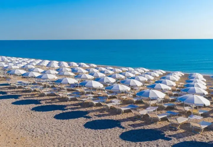 Filettate file di ombrelloni bianchi e lettini sulla spiaggia di Porto San Elpidio, con il mare azzurro sullo sfondo.