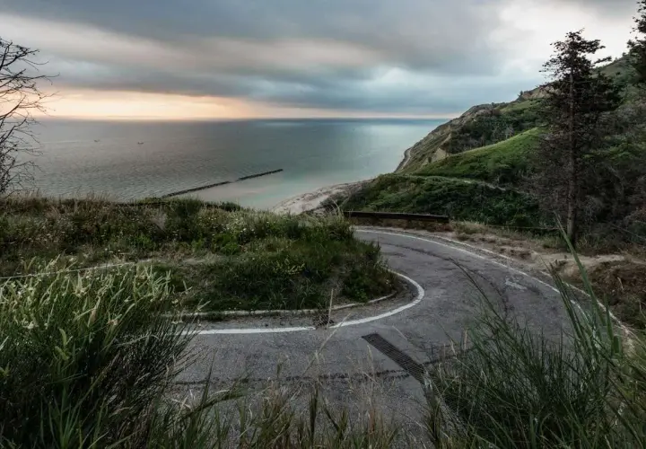 Strada panoramica che sale verso il tetto del mondo a Pesaro, con vista sul mare Adriatico e una costa verdeggiante.