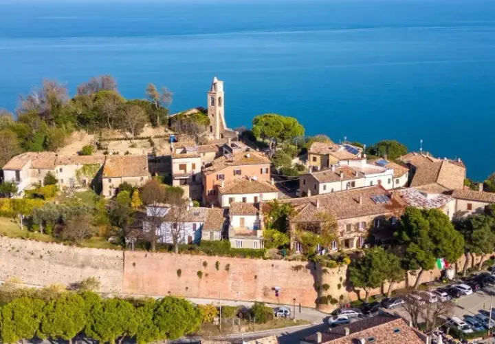Borgo medievale di Gabicce Mare cosa vedere: un incantevole panorama di case con tetti rossi, un campanile e il blu del mare Adriatico.