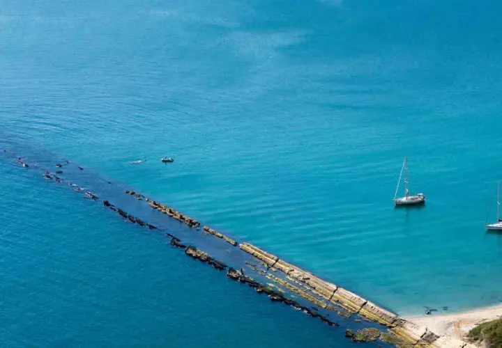 La spiaggia del Trave, con le sue acque cristalline, ospita due barche a vela e un piccolo motoscafo.