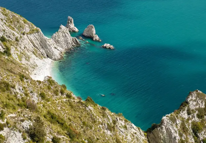 Scogliere bianche e mare cristallino del Conero, con una piccola spiaggia nascosta e un nuotatore solitario.