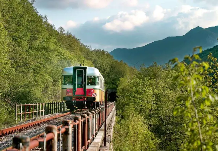 Treno d'epoca attraversa un viadotto immerso nel verde, tra Fabriano e Ancona, dirigendosi verso un tunnel tra le montagne.