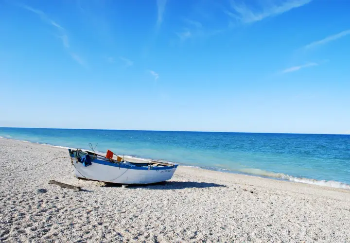 Barca bianca e blu sulla spiaggia di ciottoli a Senigallia, mare calmo e cielo azzurro.