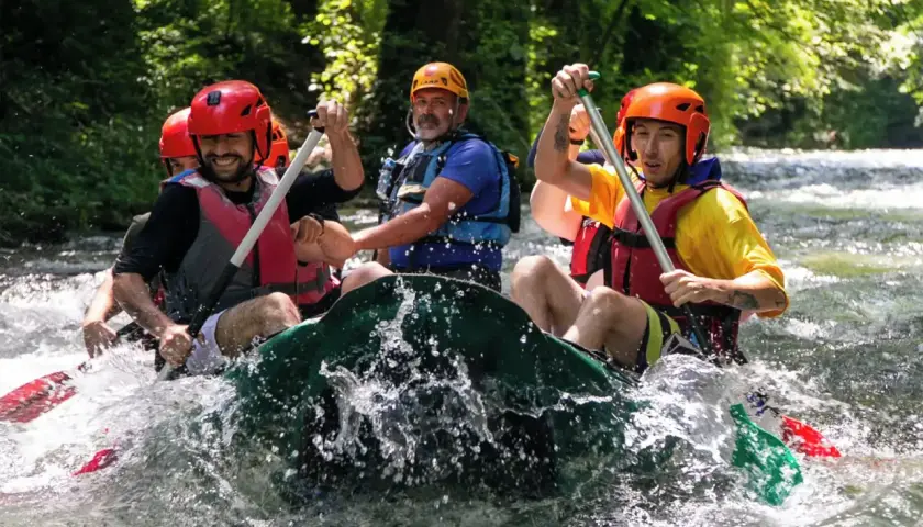 Un gruppo di amici si diverte in un'avventura di rafting nelle Marche, pagaiando con entusiasmo tra le rapide.