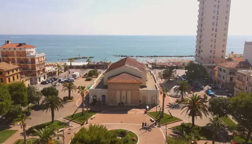 Piazza centrale con teatro, palazzi, palme e mare sullo sfondo. Ecco cosa vedere a Porto Recanati.