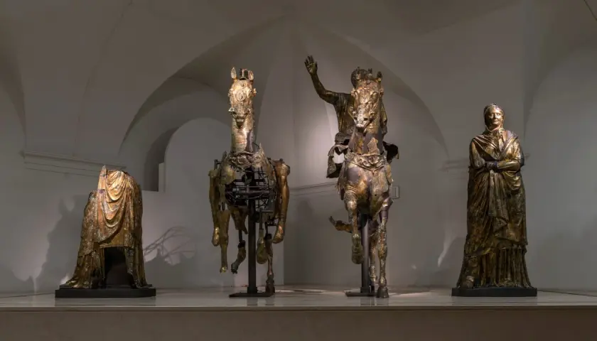 Statue equestri e figure umane in bronzo dorato, un'antica **pergola** che evoca le Marche.