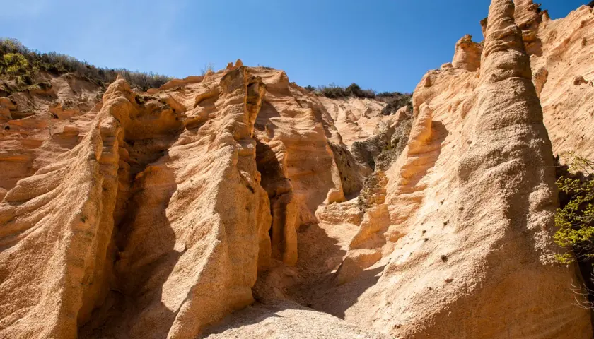 Formazioni rocciose color ocra, scolpite dal vento, sembrano **le lame rosse** di un canyon desertico sotto un cielo azzurro intenso.