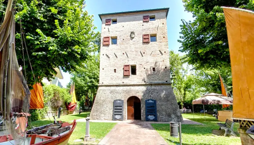 Torre dell'orologio nel centro storico di Igea Marina, con barche e bandiere colorate.