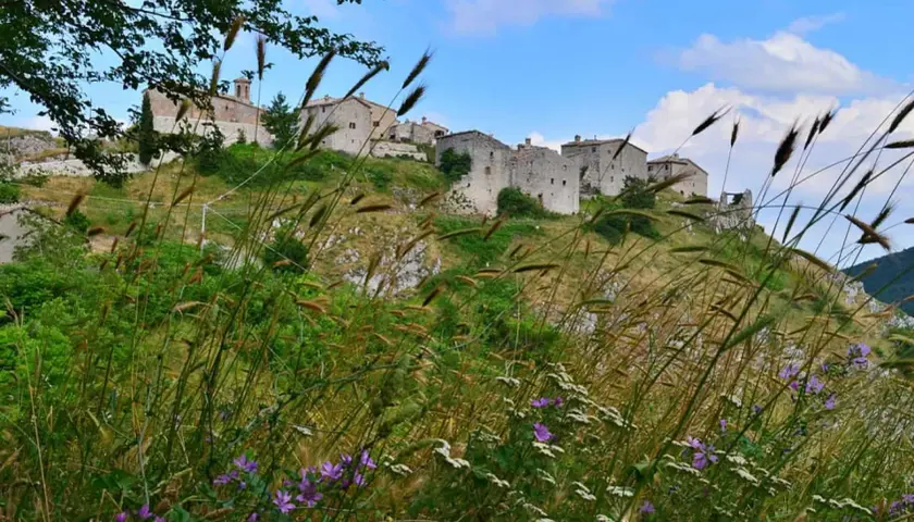 Borgo antico sui colli marchigiani, con case in pietra e vegetazione rigogliosa. Un paesaggio da cartolina, un vero gioiello dell'elcito Marche.