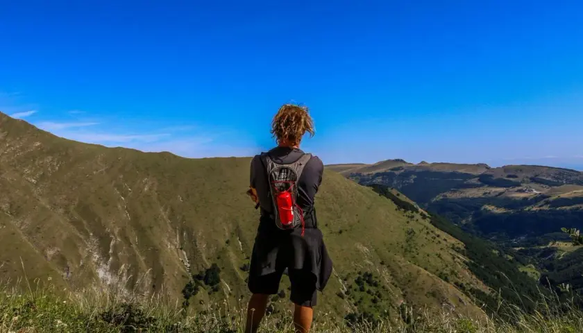 Persona con zaino ammira il panorama durante un trekking di 3 giorni nei Monti Sibillini.